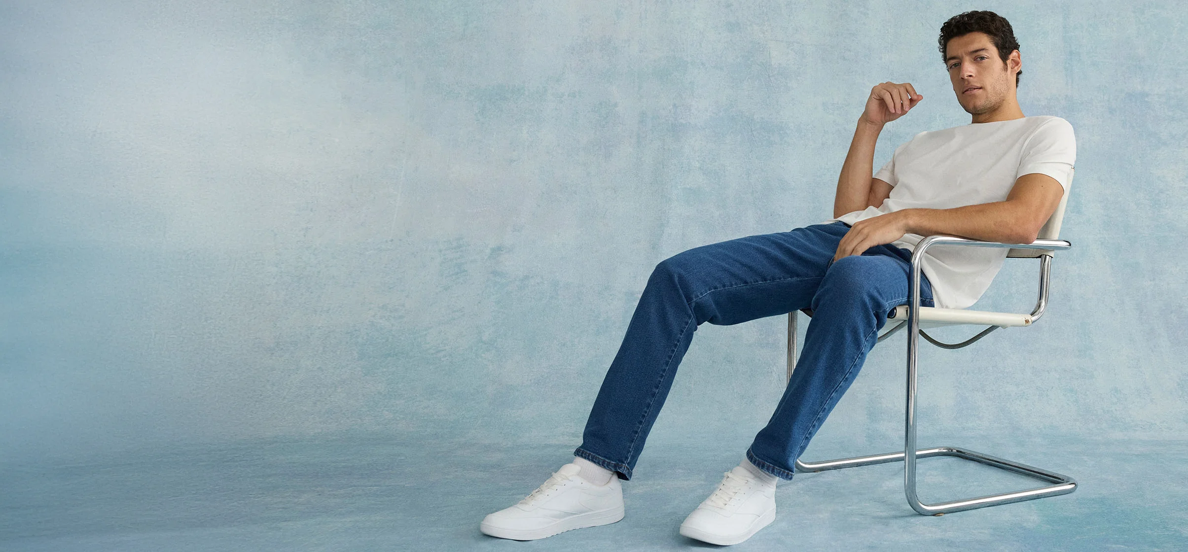 Ležérní outfit: bílé tričko, modré džíny a bílé tenisky na moderní židli.