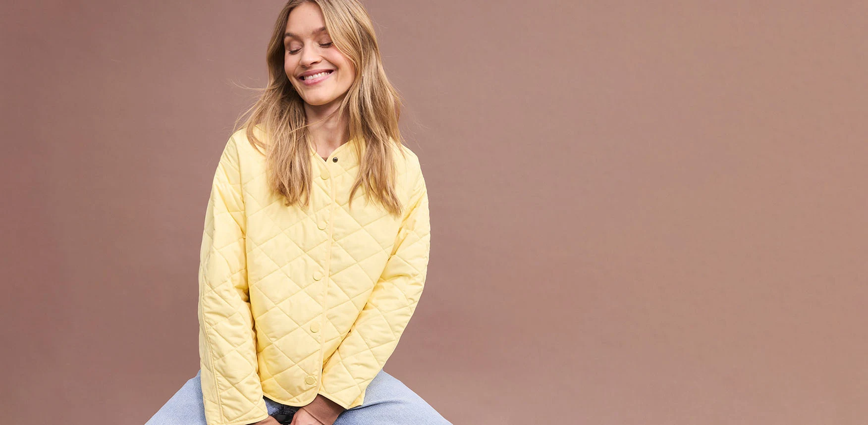 Žlutá oversize prošívaná bunda v kombinaci s modrými kalhotami.