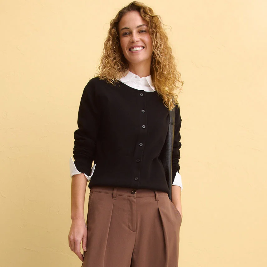 Černý svetr s knoflíky přes bílou blůzu, kombinovaný s hnědými kalhotami.