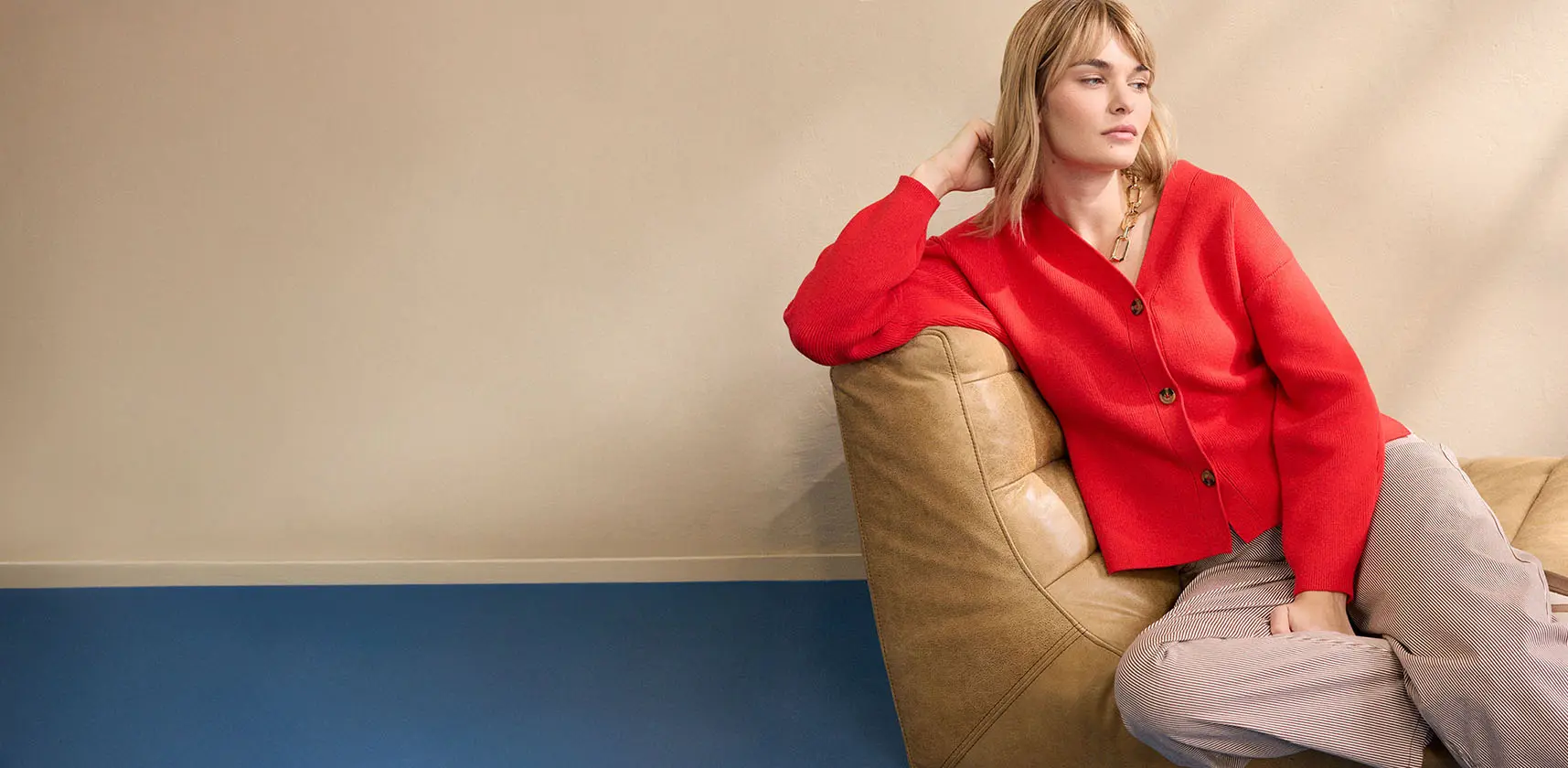 Žena má na sobě červený pletený svetr v kombinaci s béžovými kalhotami.