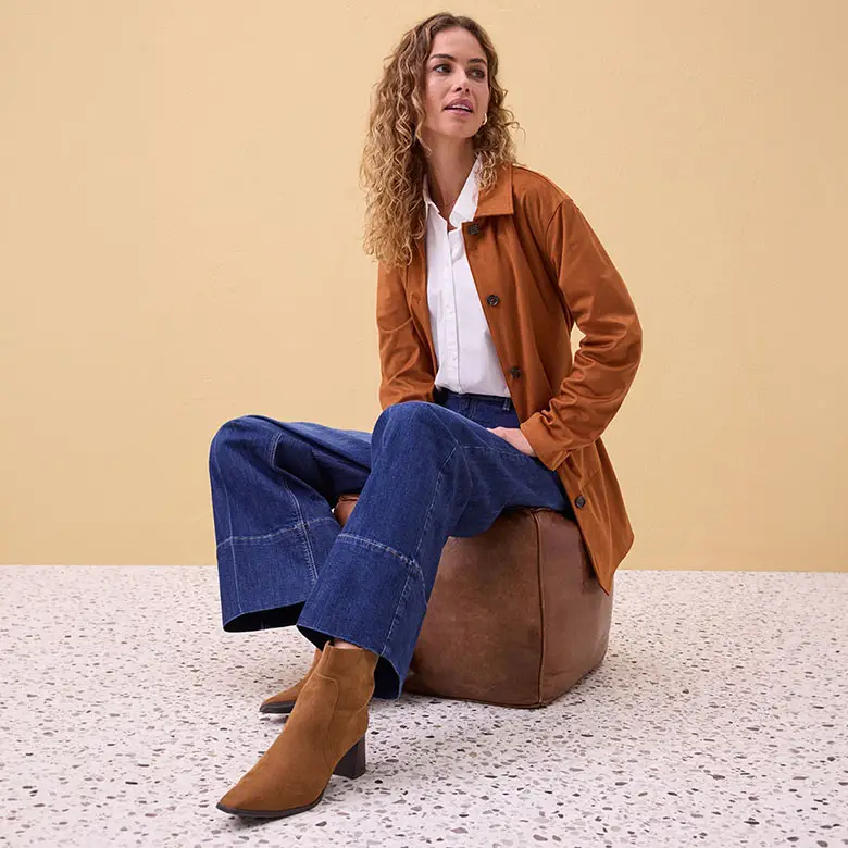 Kabát v koňakové barvě, bílá halenka, široké džíny a hnědé nízké kozačky.