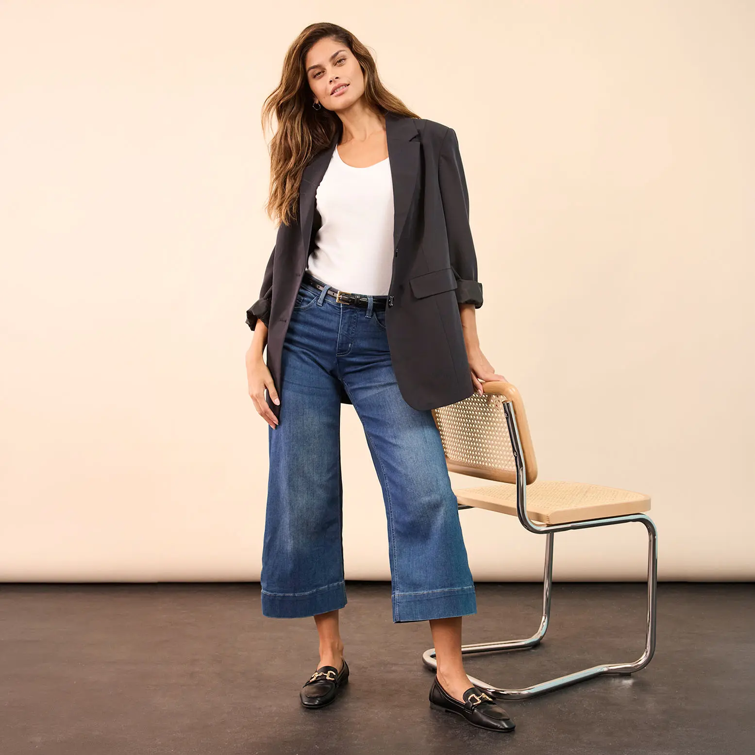 Elegantní šedé sako v kombinaci s bílým topem, širokými džínami a černými mokasíny.