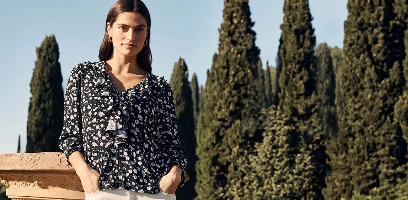 Kombinace vzorované halenky a bílých kalhot.