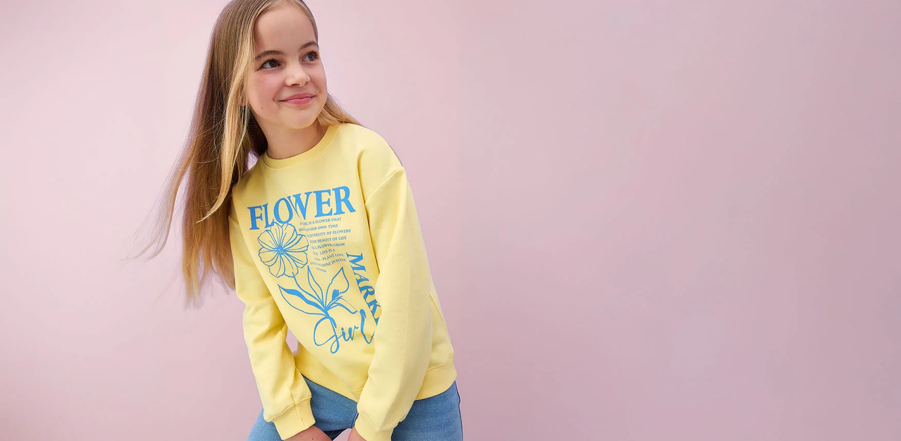 Žluté tričko s dlouhým rukávem a s květovaným vzorem, modré džíny a kšiltovka.