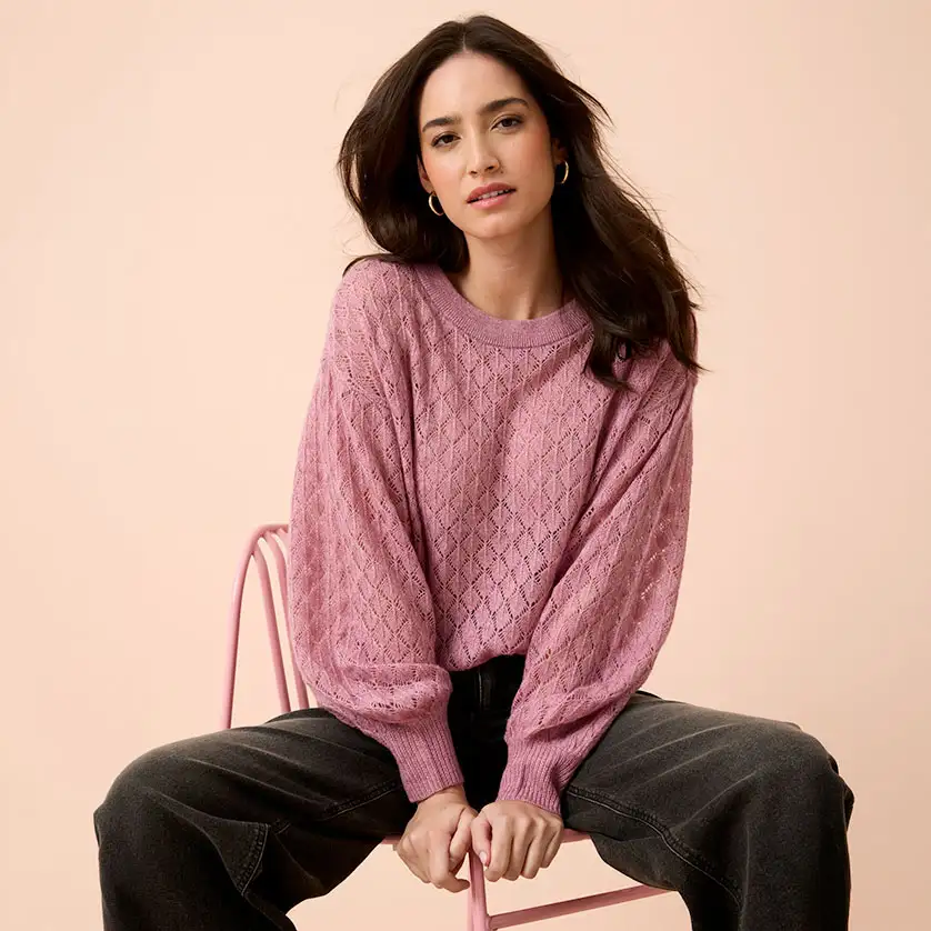 Měkký růžový pletený svetr s copánkovým vzorem v kombinaci s širokými, tmavými džínami.