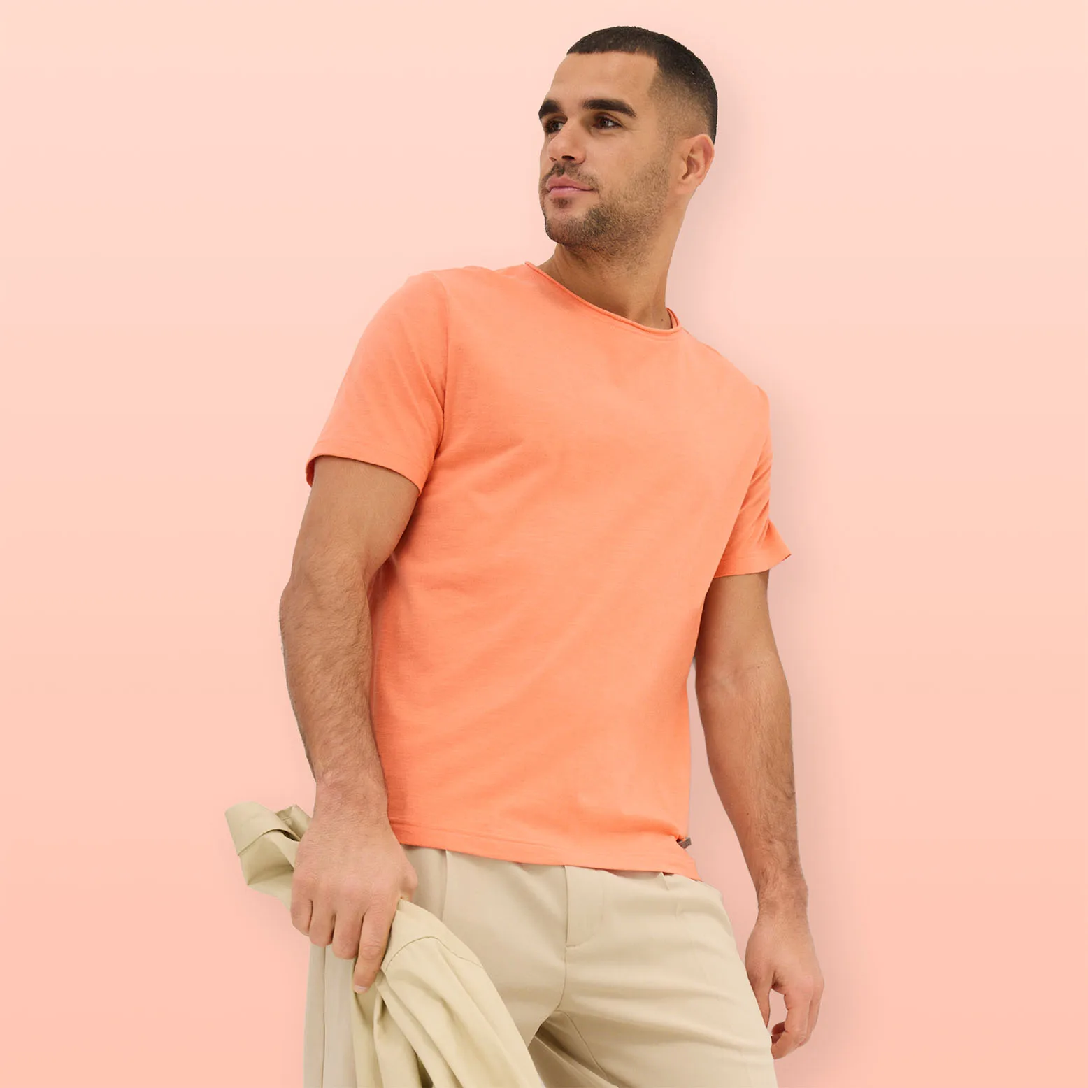 Tričko v broskvové barvě, zkombinované se světlými kalhotami a sladěným svetrem v roli doplňku.