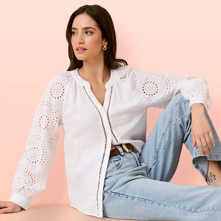 Bílá halenka s dírkovanou výšivkou a dlouhým rukávem, v kombinaci se světle modrými džínami a opaskem.