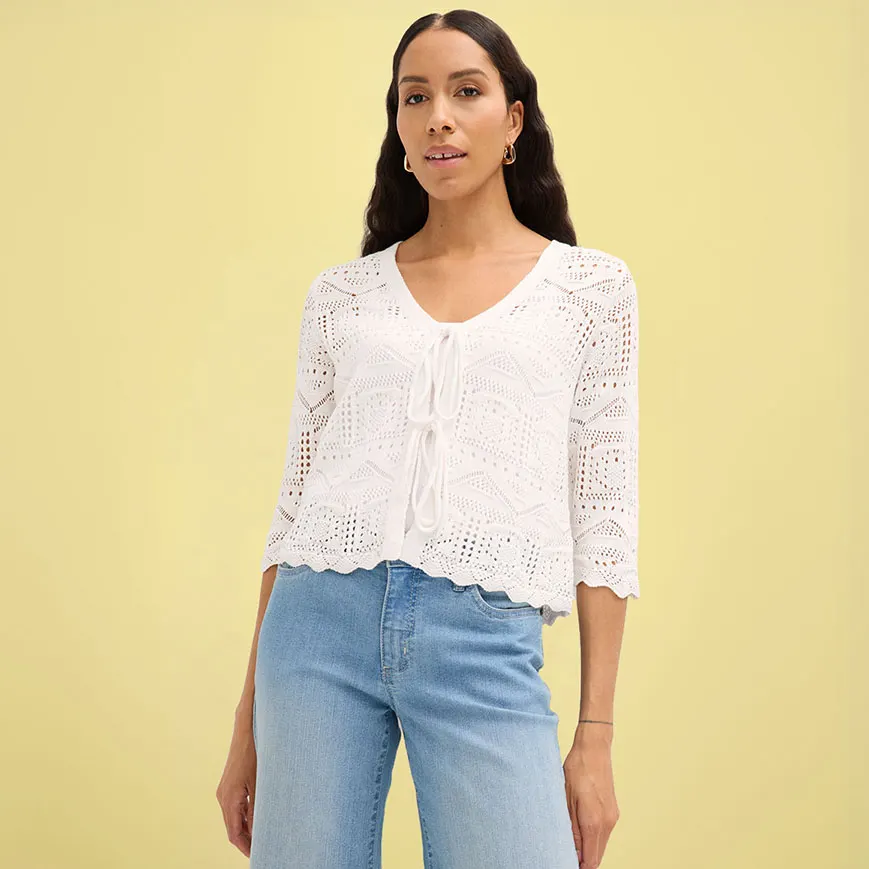 Bílý háčkovaný kabátek s polodlouhým rukávem, v kombinaci s modrými džínami.