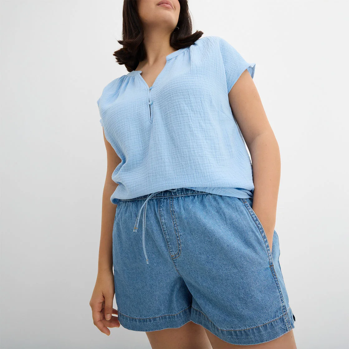 Světle modrý top bez rukávů se zipem a volné džínové šortky ve volném letním outfitu.