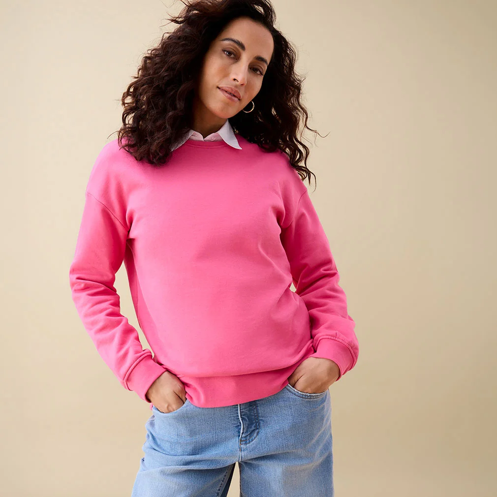 Pink mikina přes bílou košili v kombinaci s ležérními modrými džínami.