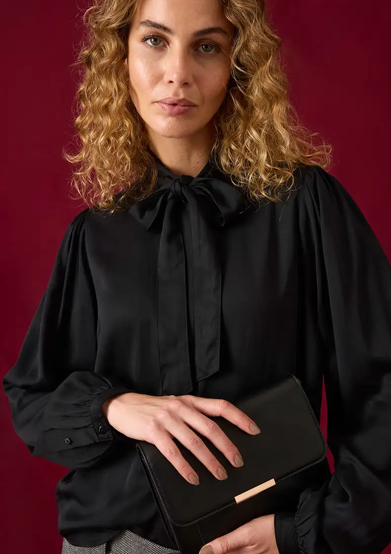 Černá halenka s elegantní mašlí a širokými rukávy, v kombinaci se stylovým psaníčkem.