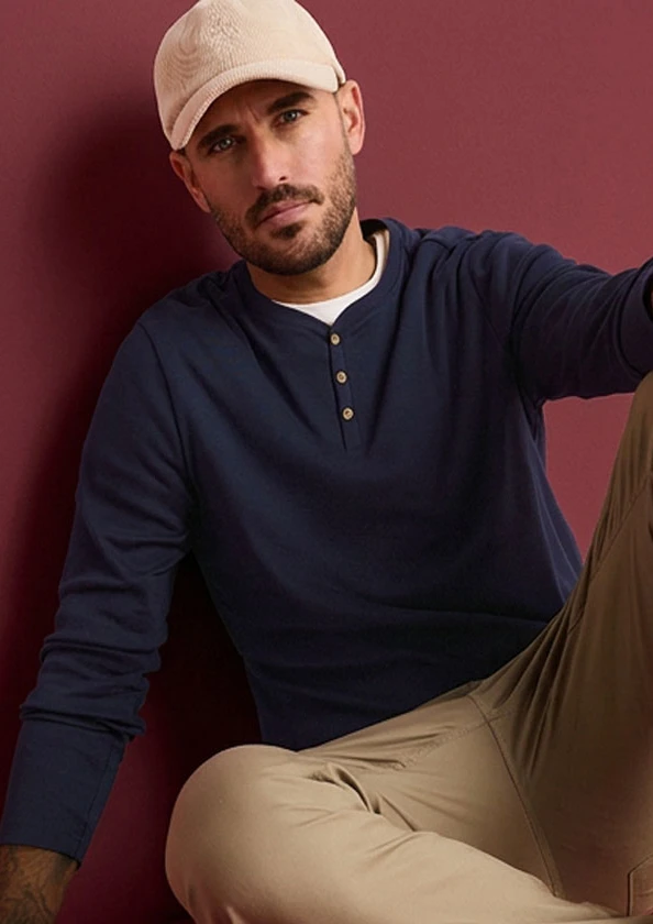 Muž má na sobě béžovou kšiltovku, námořnicky modré tričko henley a béžové kalhoty.