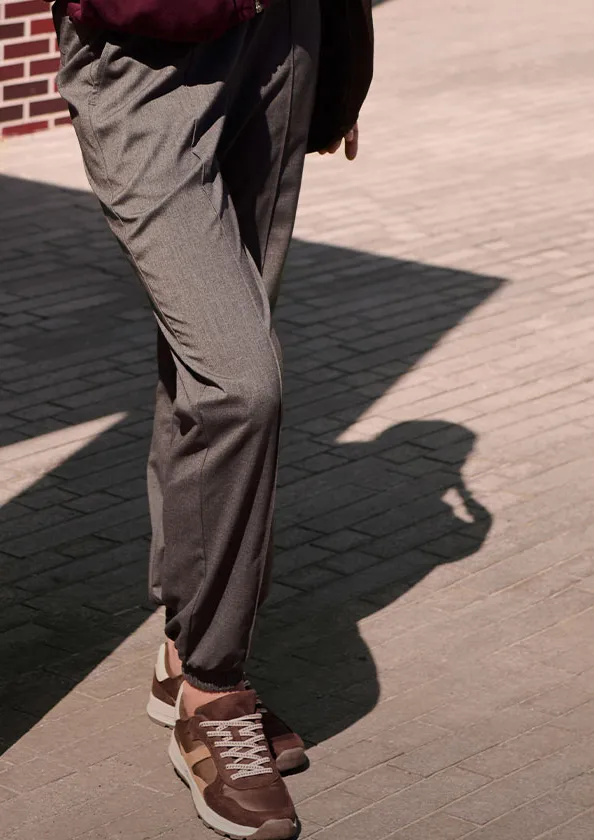 Šedé látkové kalhoty a hnědé tenisky vyzařují ležérně elegantní styl.